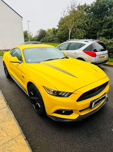 An image of a yellow car parked outside with other cars